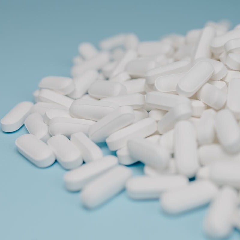 Close-up of white pills scattered on a blue background, focusing on pharmaceuticals.