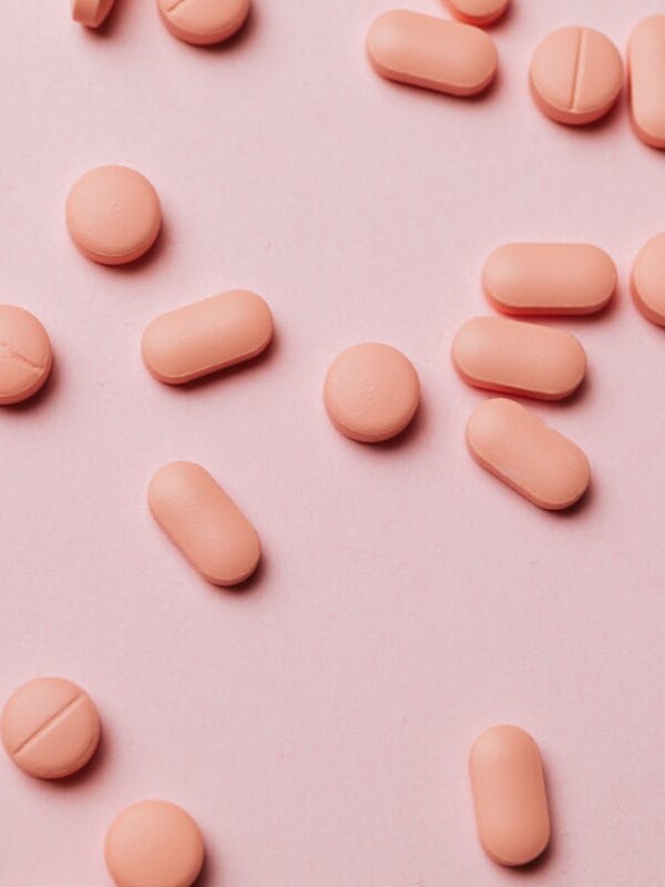 Flat lay photo of pink pills on a pastel pink background, ideal for pharmaceutical themes.