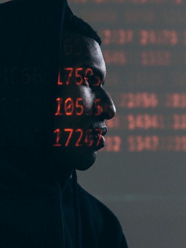 Side profile of a man in a hoodie, surrounded by red code, depicting cybersecurity theme.