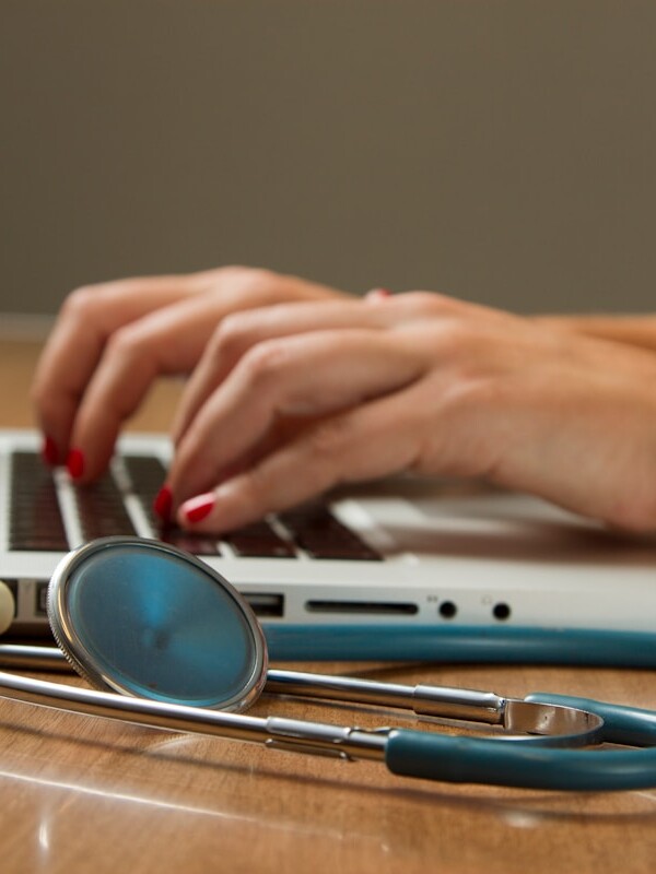 person sitting while using laptop computer and green stethoscope near