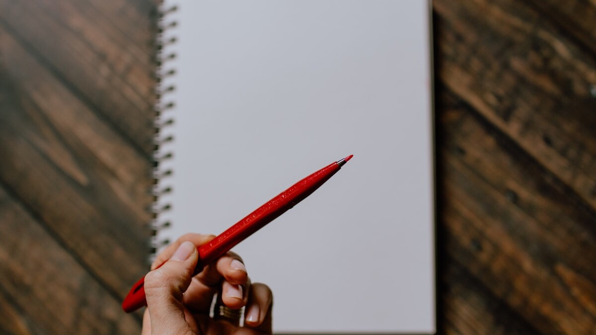 person holding red pencil writing on white paper