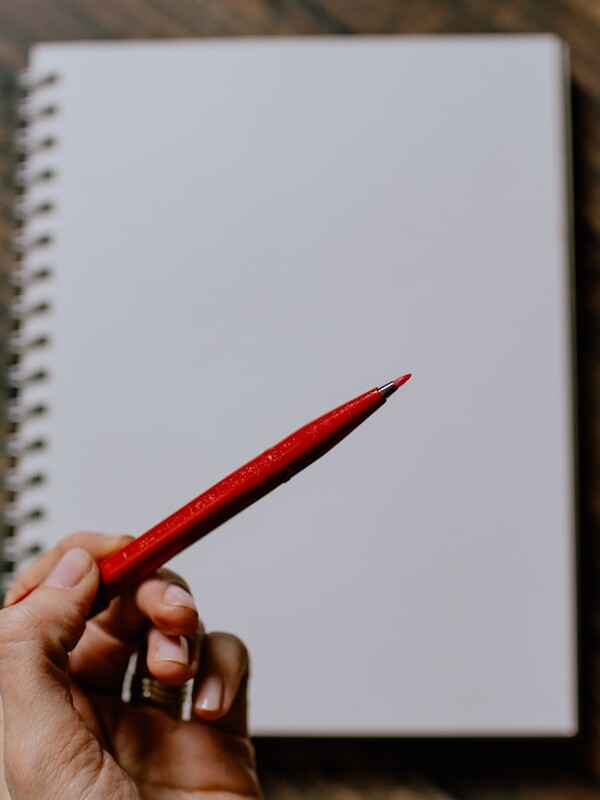 person holding red pencil writing on white paper